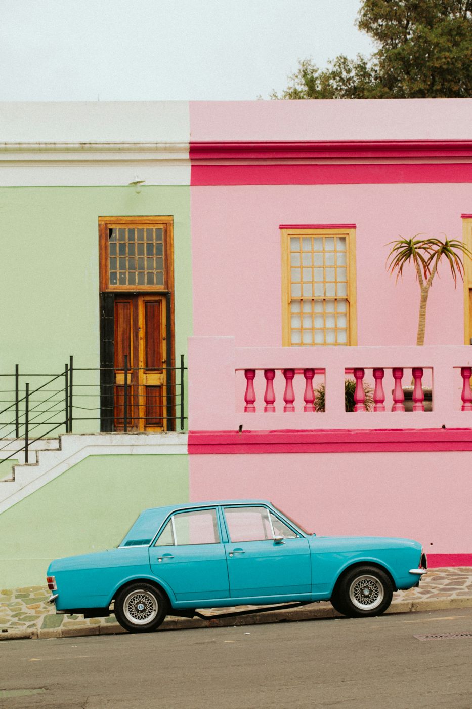 A blue vintage car outside pink and green houses